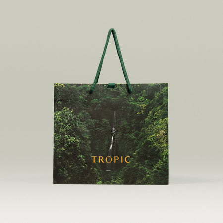 Tropic Skincare reusable gift bag with rainforest design and green rope handles, featuring a waterfall image and the Tropic logo in gold.